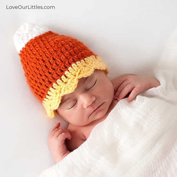 Sleeping baby wearing a candy corn Halloween hat for Halloween photos.