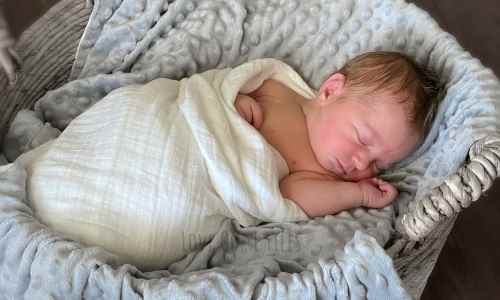 Newborn posing on the back, wrapped in a swaddle and lying asleep in a basket.