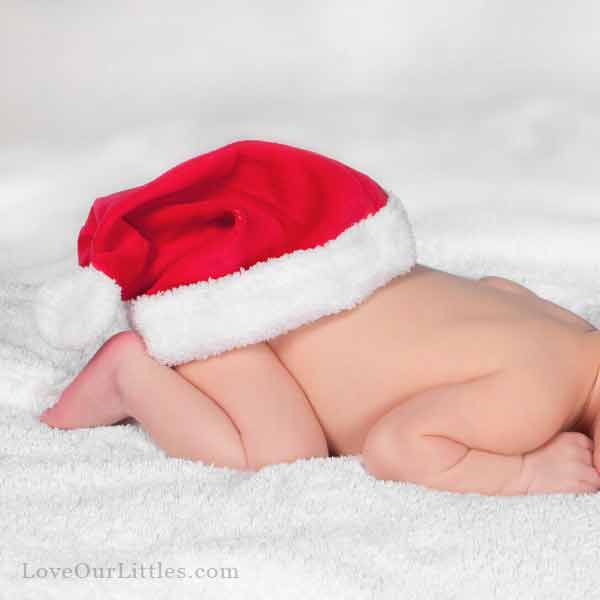 A Christmas photo of a newborn baby lying on her stomach with a Santa hat placed on her bottom.