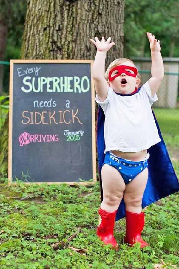 Toddler boy dressed as a superhero announcing his mom's pregnancy.